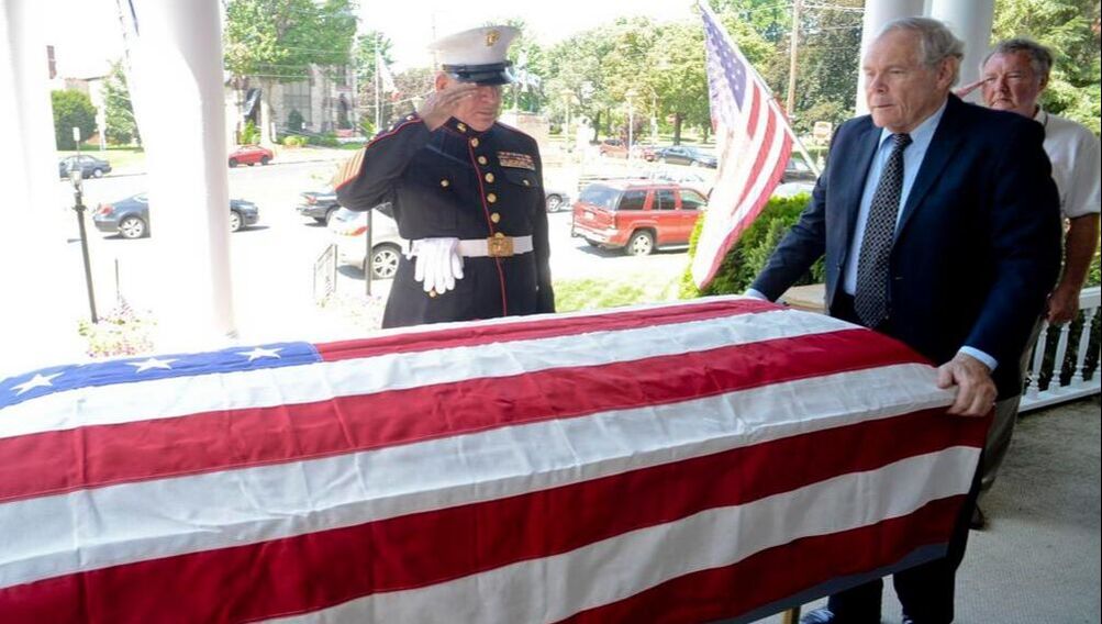 Mike Feeney, director and veteran assists with carrying of flag draped casket.