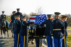 Military personnel carry a casket drapped with the American Flag.