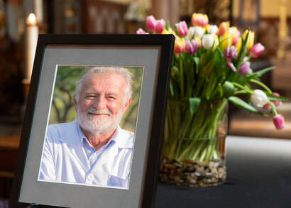 Table with picture frame, with photo of a man, and a vase of tulips.